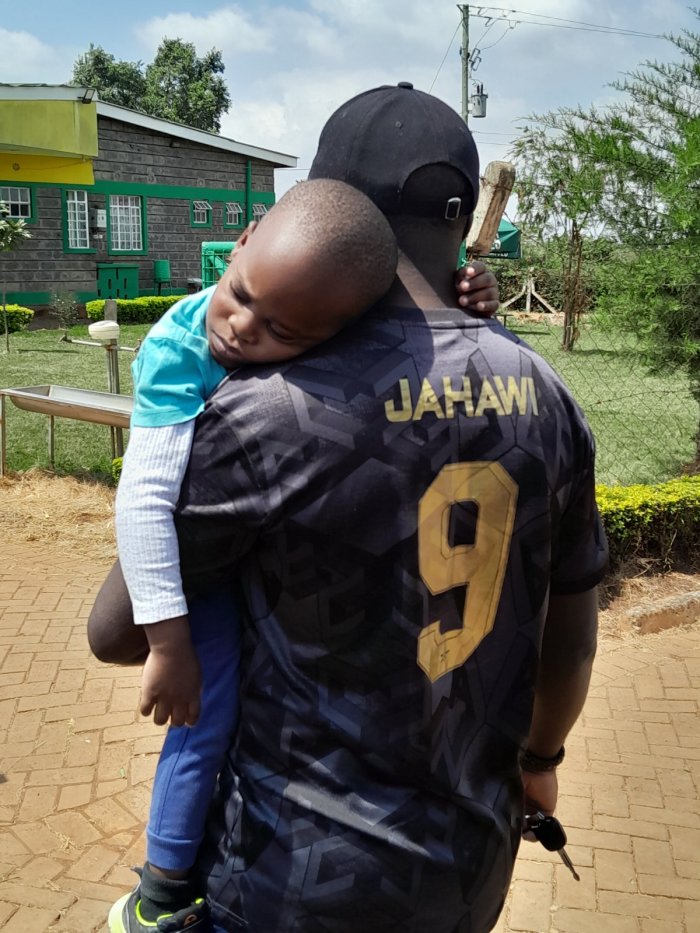 Haron Owalo carrying a sleeping child, a quiet family moment